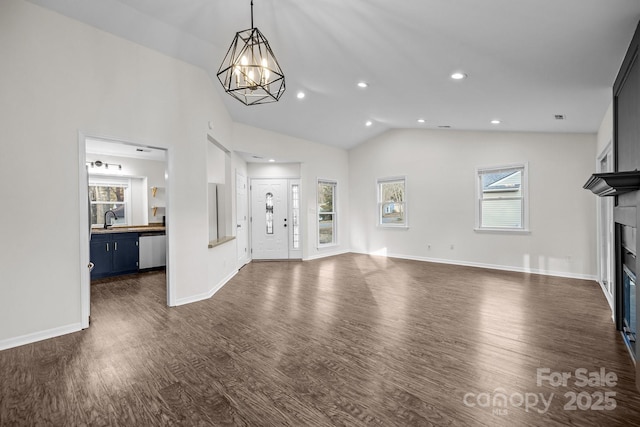 unfurnished living room with dark wood-style floors, a fireplace, lofted ceiling, a sink, and baseboards