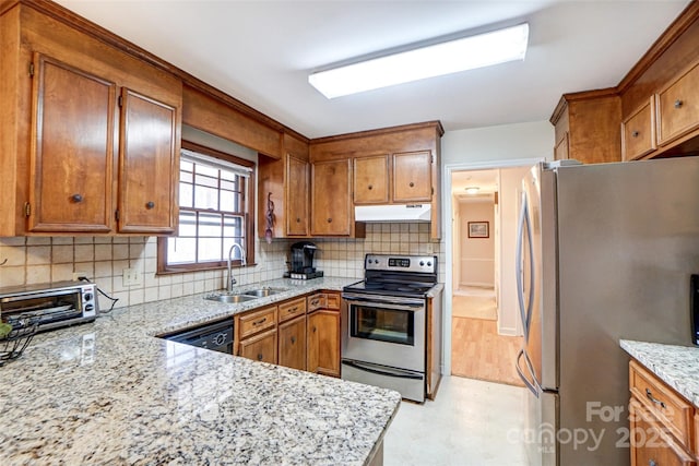 kitchen featuring a toaster, under cabinet range hood, stainless steel appliances, a sink, and brown cabinetry