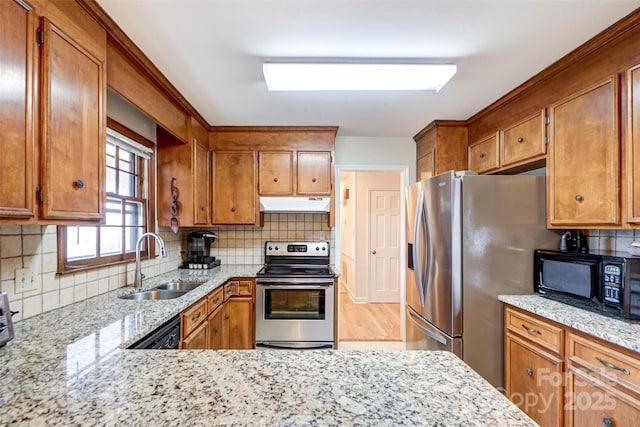 kitchen with brown cabinets, backsplash, a sink, under cabinet range hood, and black appliances