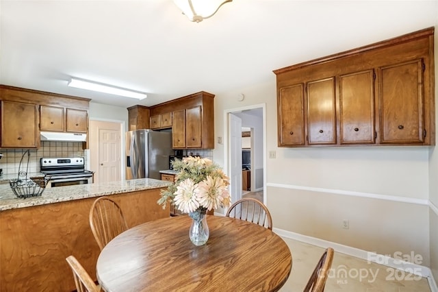 kitchen featuring baseboards, decorative backsplash, brown cabinets, stainless steel appliances, and under cabinet range hood