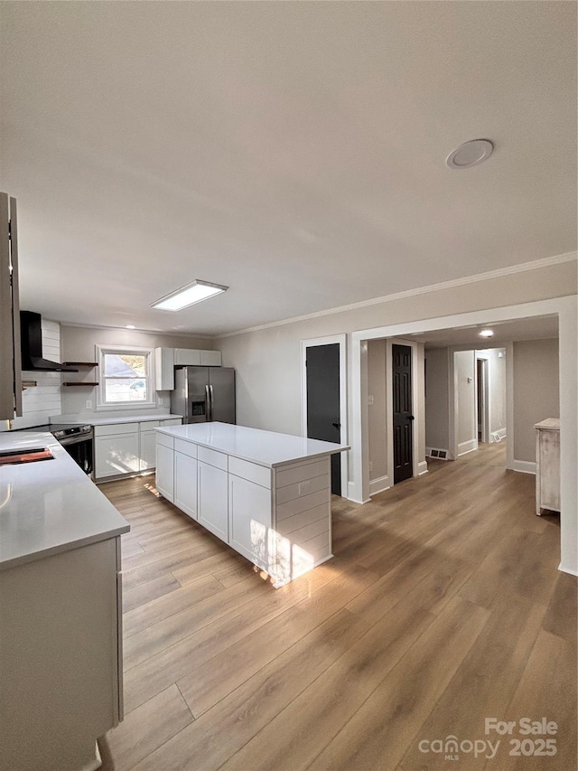 kitchen featuring a kitchen island, light countertops, light wood-type flooring, stainless steel refrigerator with ice dispenser, and crown molding