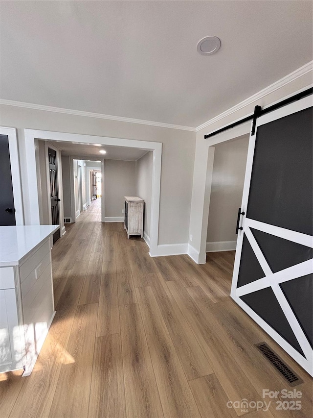 corridor featuring light wood finished floors, visible vents, a barn door, ornamental molding, and baseboards