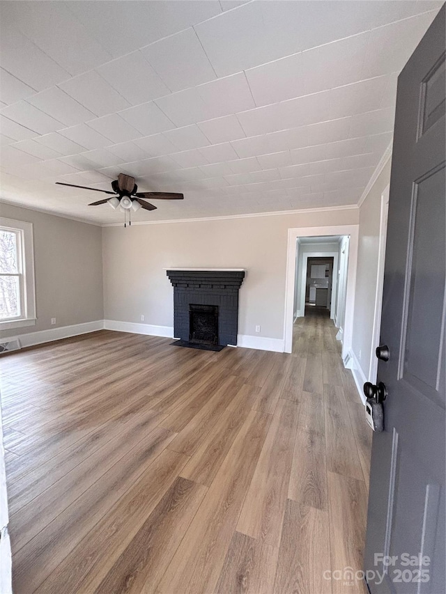 unfurnished living room with baseboards, a ceiling fan, light wood-style flooring, crown molding, and a fireplace