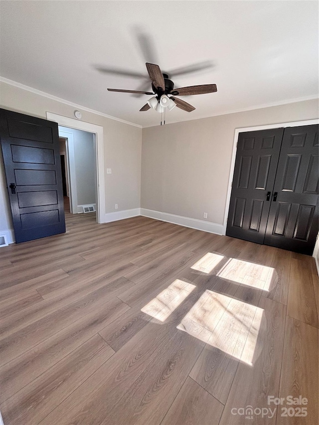 unfurnished bedroom with visible vents, ornamental molding, a ceiling fan, wood finished floors, and baseboards