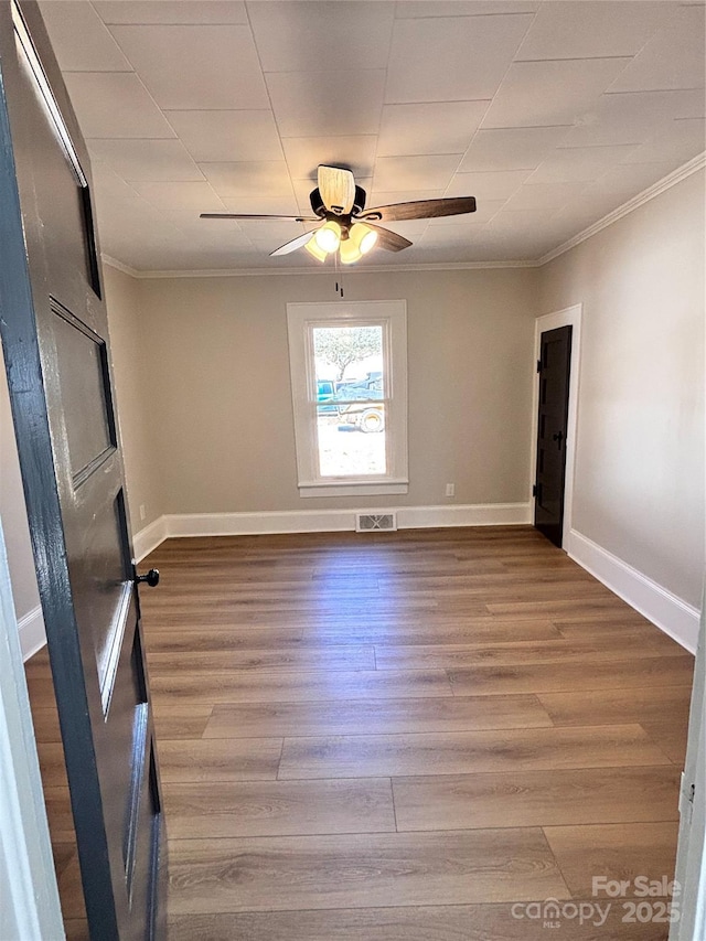 empty room featuring visible vents, crown molding, baseboards, and wood finished floors