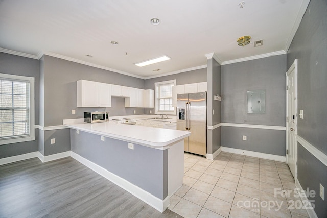 kitchen with electric panel, appliances with stainless steel finishes, a peninsula, light countertops, and a sink