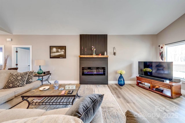 living room featuring a fireplace, baseboards, vaulted ceiling, and wood finished floors