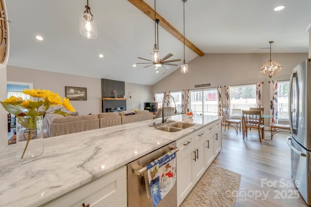 kitchen with light wood finished floors, a sink, light stone countertops, stainless steel appliances, and beam ceiling