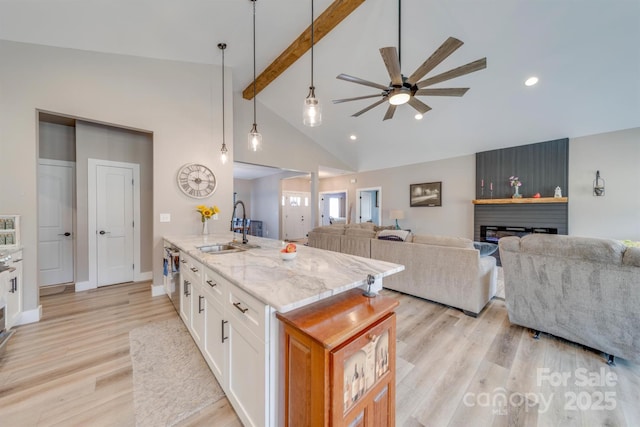 kitchen with white cabinets, light wood-style flooring, light stone counters, a fireplace, and a sink