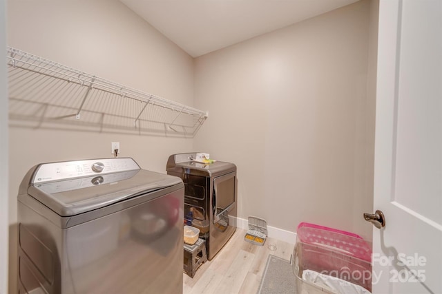 laundry area with laundry area, washing machine and dryer, baseboards, and wood finished floors