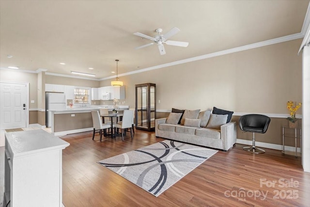 living area featuring a ceiling fan, baseboards, wood finished floors, and ornamental molding
