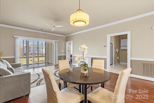 dining area featuring visible vents, light wood-style floors, ornamental molding, ceiling fan, and baseboards