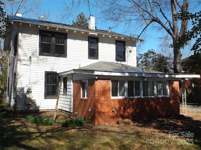 rear view of property featuring brick siding and a chimney