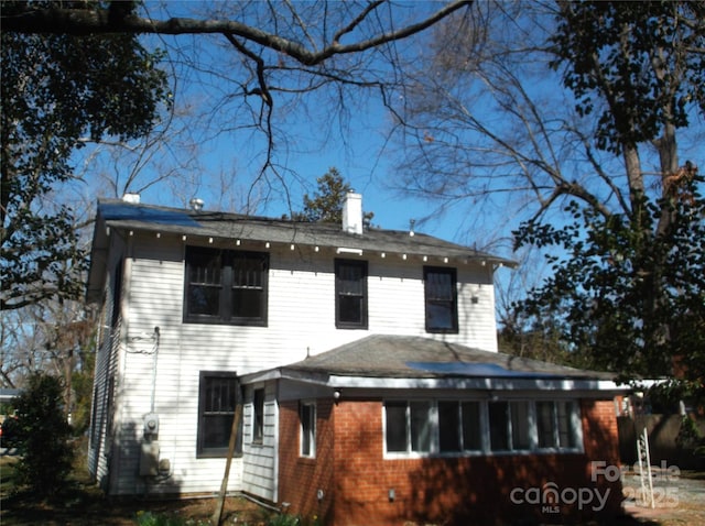 rear view of house featuring brick siding and a chimney