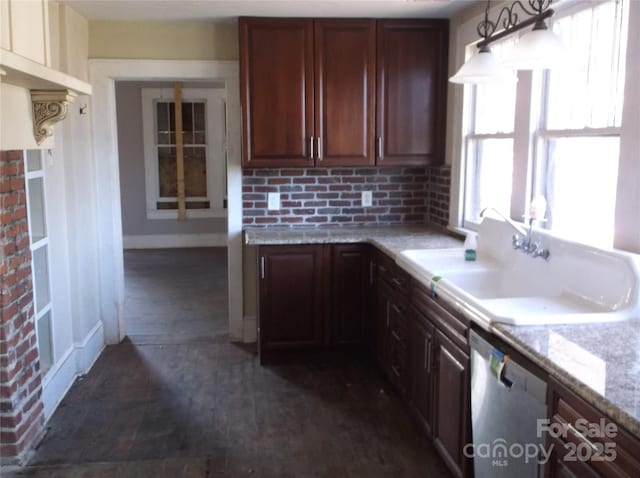 kitchen with decorative light fixtures, stainless steel dishwasher, a sink, light stone countertops, and baseboards