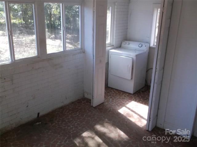 washroom with laundry area, brick floor, brick wall, and washer / dryer