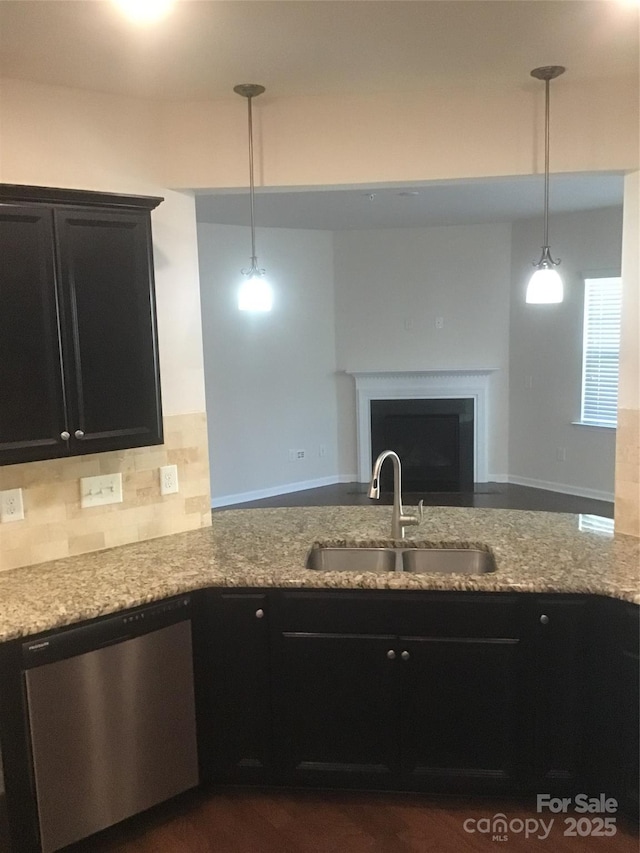 kitchen with a sink, stainless steel dishwasher, dark cabinetry, a peninsula, and light stone countertops