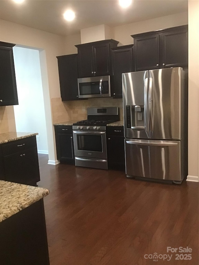 kitchen featuring stainless steel appliances, light stone countertops, dark wood-type flooring, and dark cabinetry