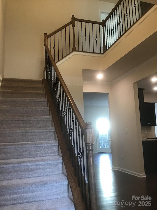 staircase with crown molding, wood finished floors, baseboards, and a towering ceiling