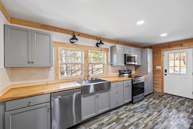 kitchen with stainless steel appliances, gray cabinets, butcher block counters, decorative backsplash, and a sink