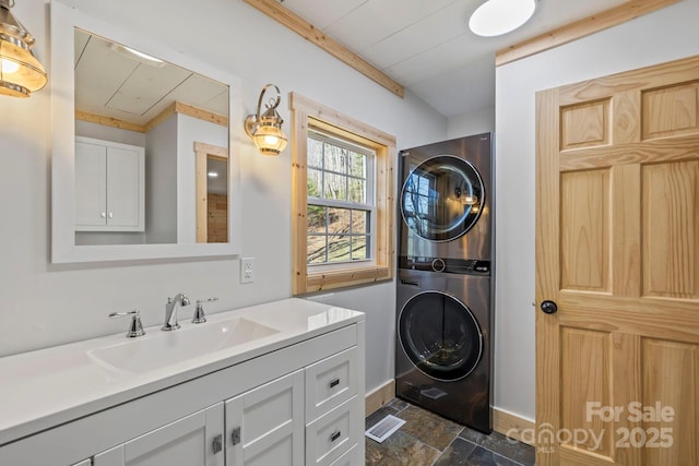 bathroom featuring stone finish flooring, vanity, stacked washer and clothes dryer, and baseboards