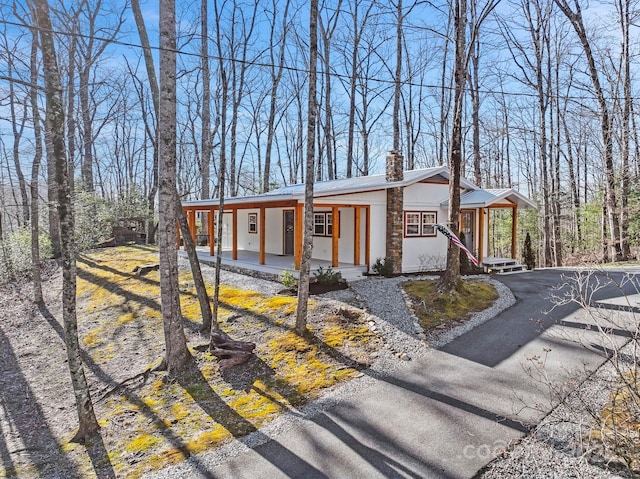 view of front of home with metal roof, driveway, a porch, and a chimney