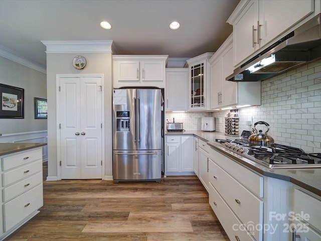 kitchen featuring under cabinet range hood, white cabinets, appliances with stainless steel finishes, glass insert cabinets, and crown molding