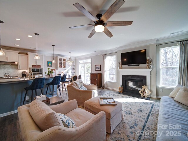 living room featuring crown molding, a glass covered fireplace, ceiling fan, wood finished floors, and baseboards