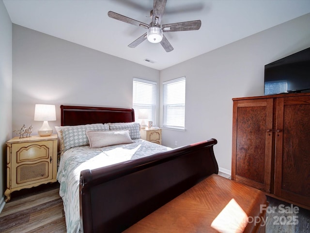 bedroom with a ceiling fan, visible vents, baseboards, and wood finished floors