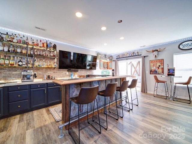 bar with light wood-style flooring, recessed lighting, visible vents, backsplash, and wet bar