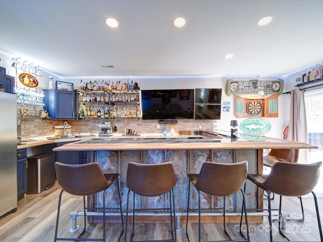 bar with light wood-type flooring, decorative backsplash, indoor wet bar, and freestanding refrigerator