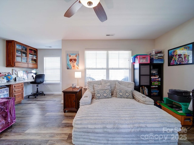 bedroom featuring visible vents, light wood-style floors, a ceiling fan, built in study area, and baseboards