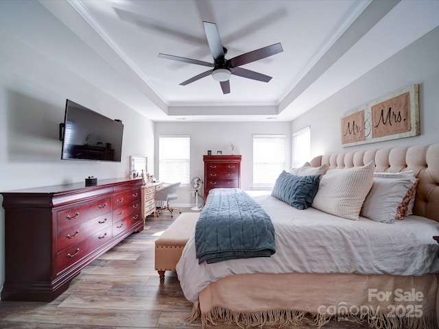 bedroom featuring a tray ceiling, multiple windows, crown molding, and wood finished floors