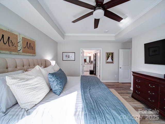 bedroom with baseboards, ensuite bath, ornamental molding, wood finished floors, and a tray ceiling