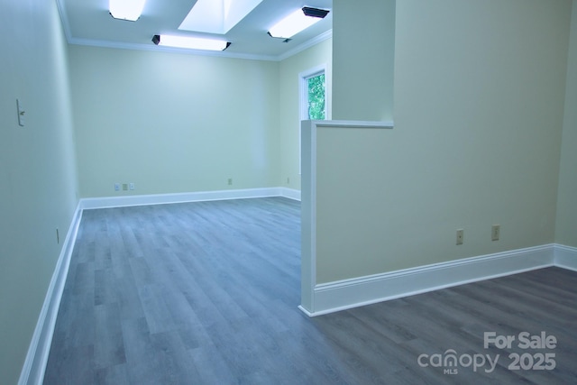 empty room with ornamental molding, a skylight, wood finished floors, and baseboards