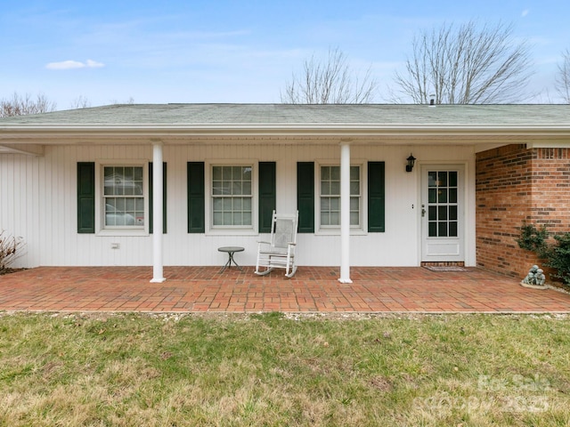 property entrance featuring a yard, roof with shingles, and brick siding