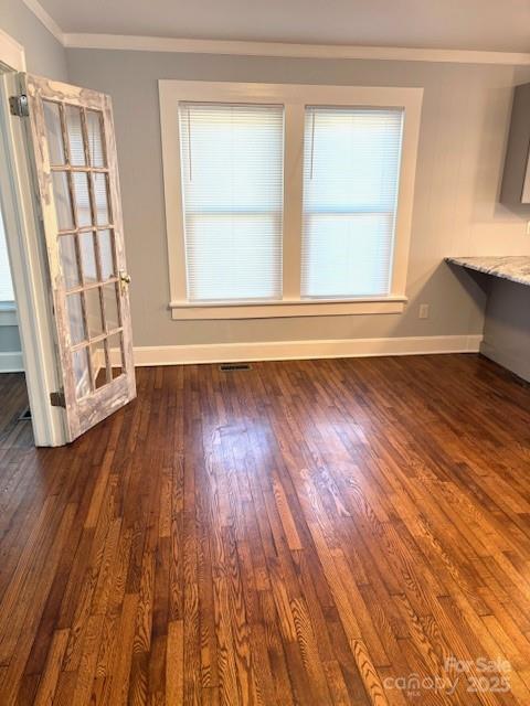 interior space with dark wood-style floors, ornamental molding, visible vents, and baseboards