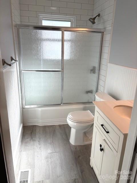 full bath featuring visible vents, wainscoting, combined bath / shower with glass door, vanity, and wood finished floors