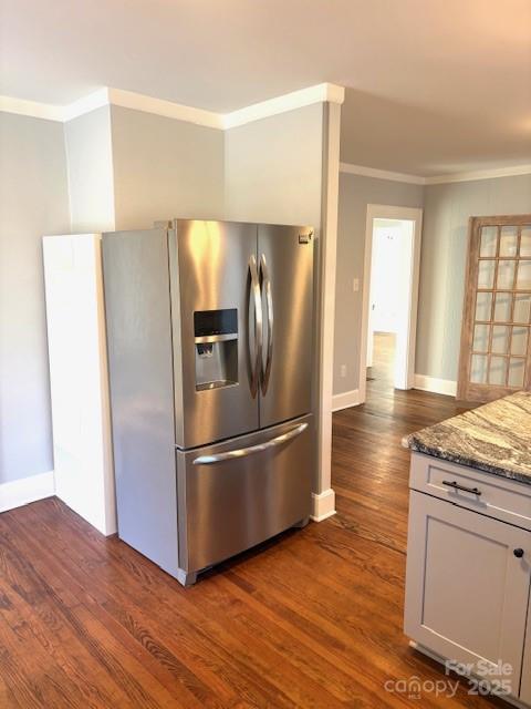 kitchen with stone counters, baseboards, ornamental molding, stainless steel fridge with ice dispenser, and dark wood finished floors