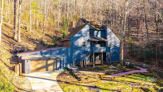 chalet / cabin with a chimney, concrete driveway, stairway, a garage, and a forest view