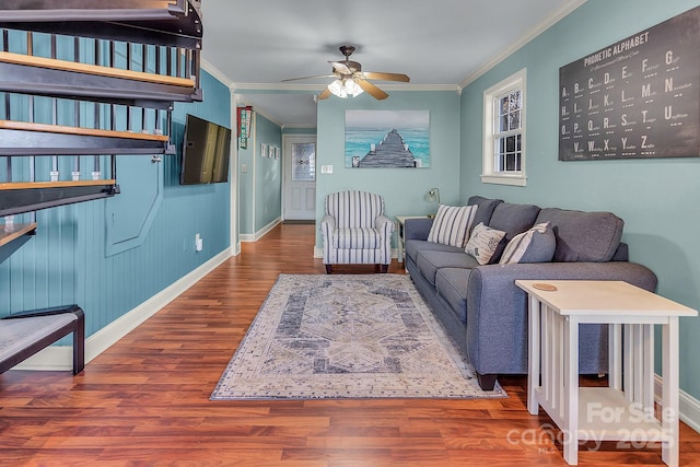 living room featuring a ceiling fan, crown molding, baseboards, and wood finished floors