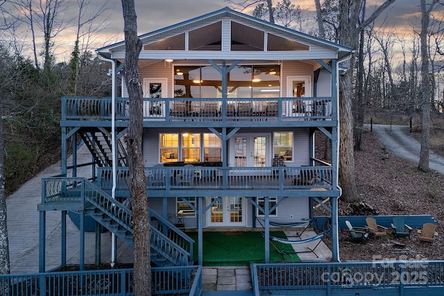 back of property at dusk featuring stairs, french doors, and a wooden deck