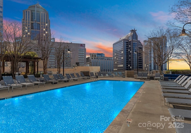 pool at dusk with a view of city, a patio area, and a community pool