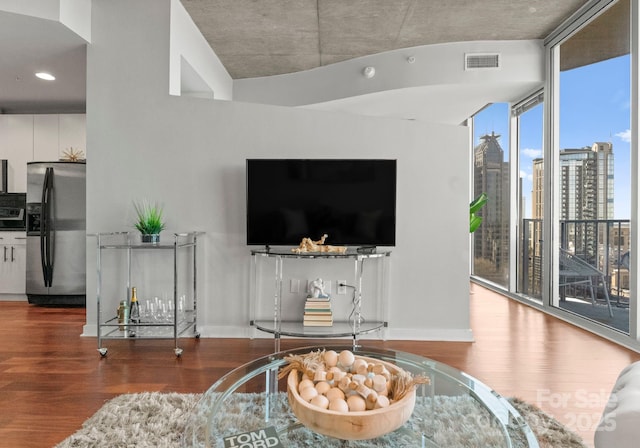 living room with a wall of windows, wood finished floors, visible vents, and baseboards