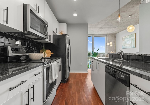 kitchen with stainless steel appliances, a sink, white cabinetry, tasteful backsplash, and dark wood finished floors