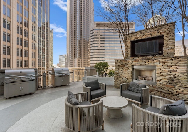 view of patio with a view of city, an outdoor stone fireplace, and grilling area