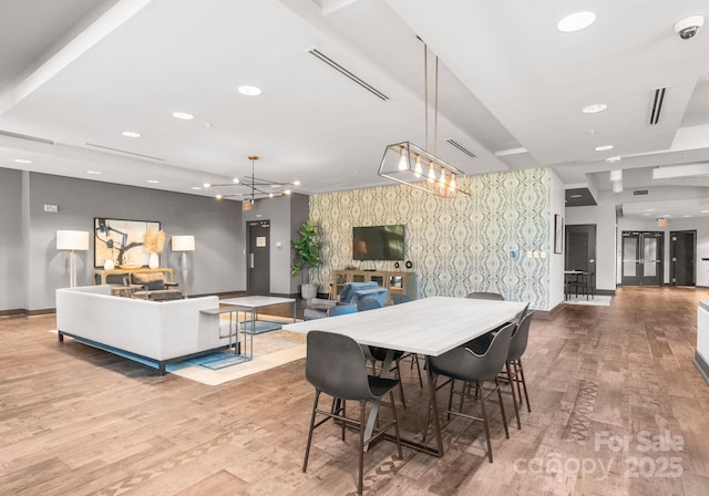 dining space with a notable chandelier, visible vents, an accent wall, wood finished floors, and wallpapered walls