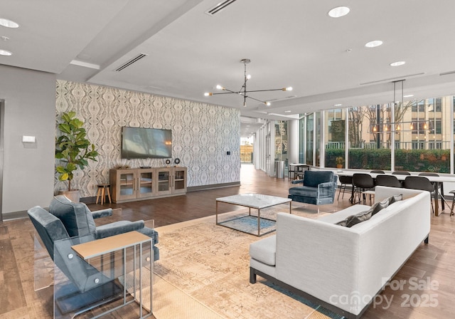 living room with a notable chandelier, an accent wall, wood finished floors, baseboards, and wallpapered walls