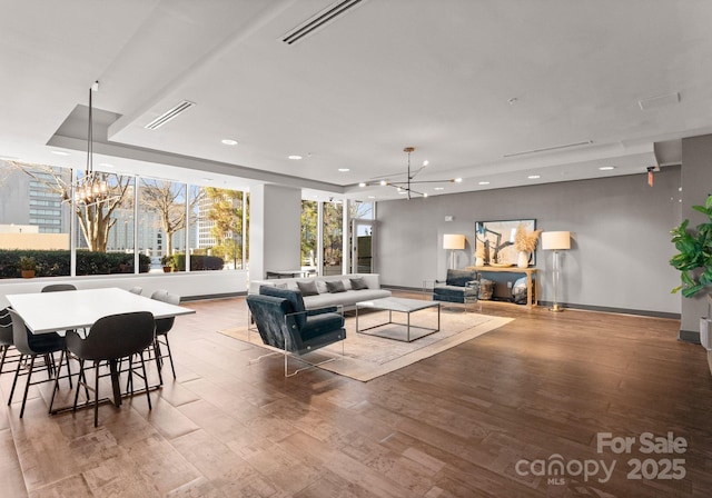 living area with visible vents, a raised ceiling, a notable chandelier, and wood finished floors