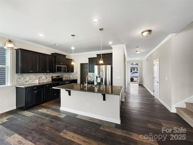 kitchen with backsplash, appliances with stainless steel finishes, an island with sink, dark stone counters, and a kitchen bar